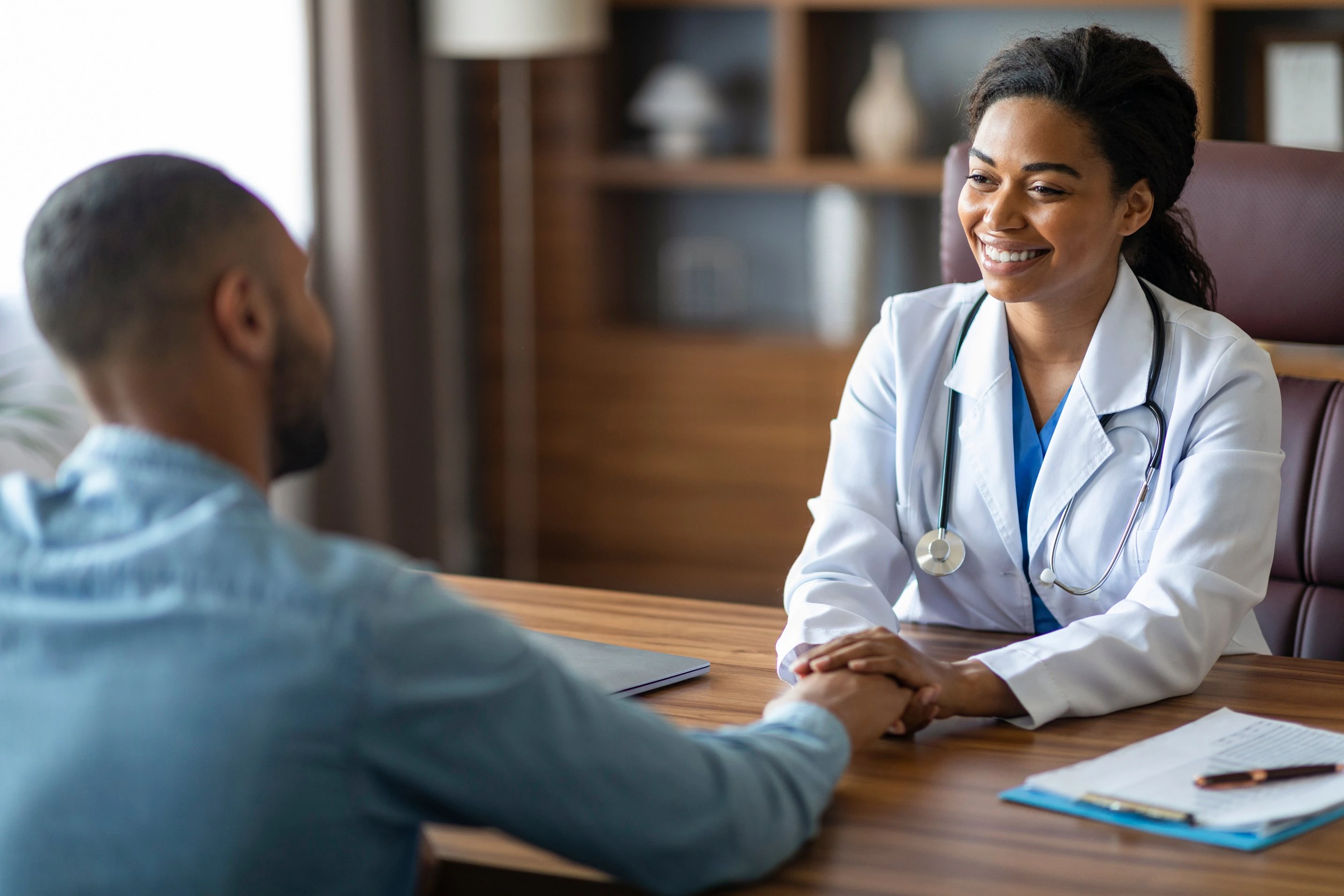 A doctor holding a patient’s hands across a desk during a consultation