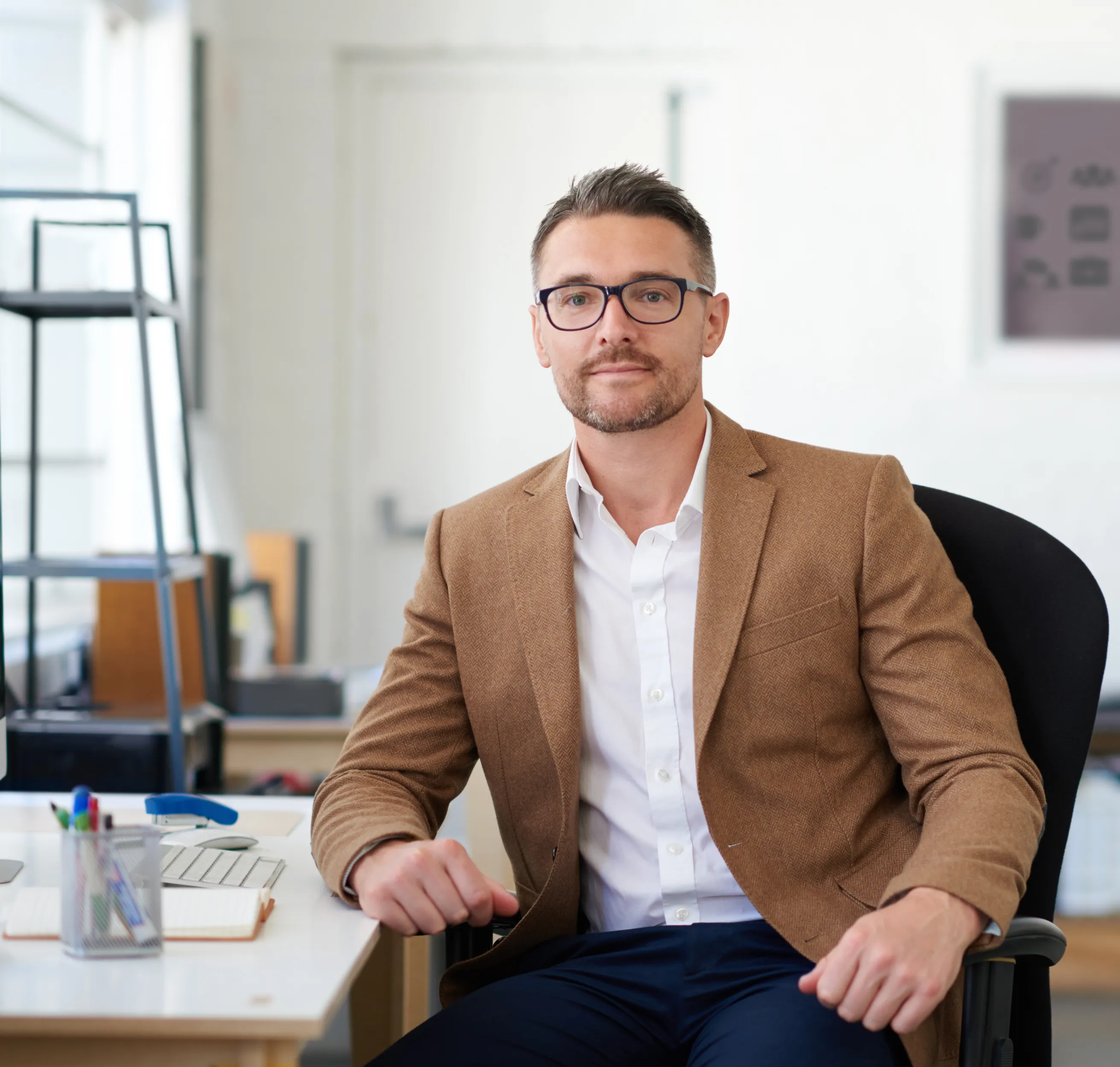 A person in glasses and a tweed jacket seated in an office